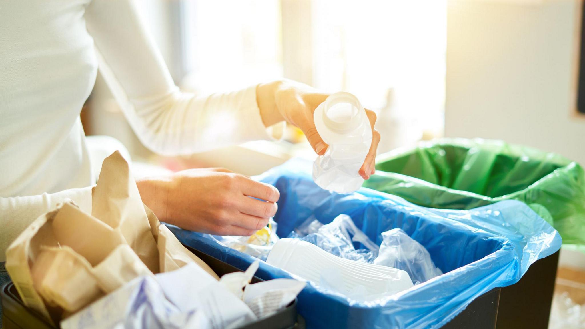 A woman in a white top sorting recyclable waste into three different boxes.