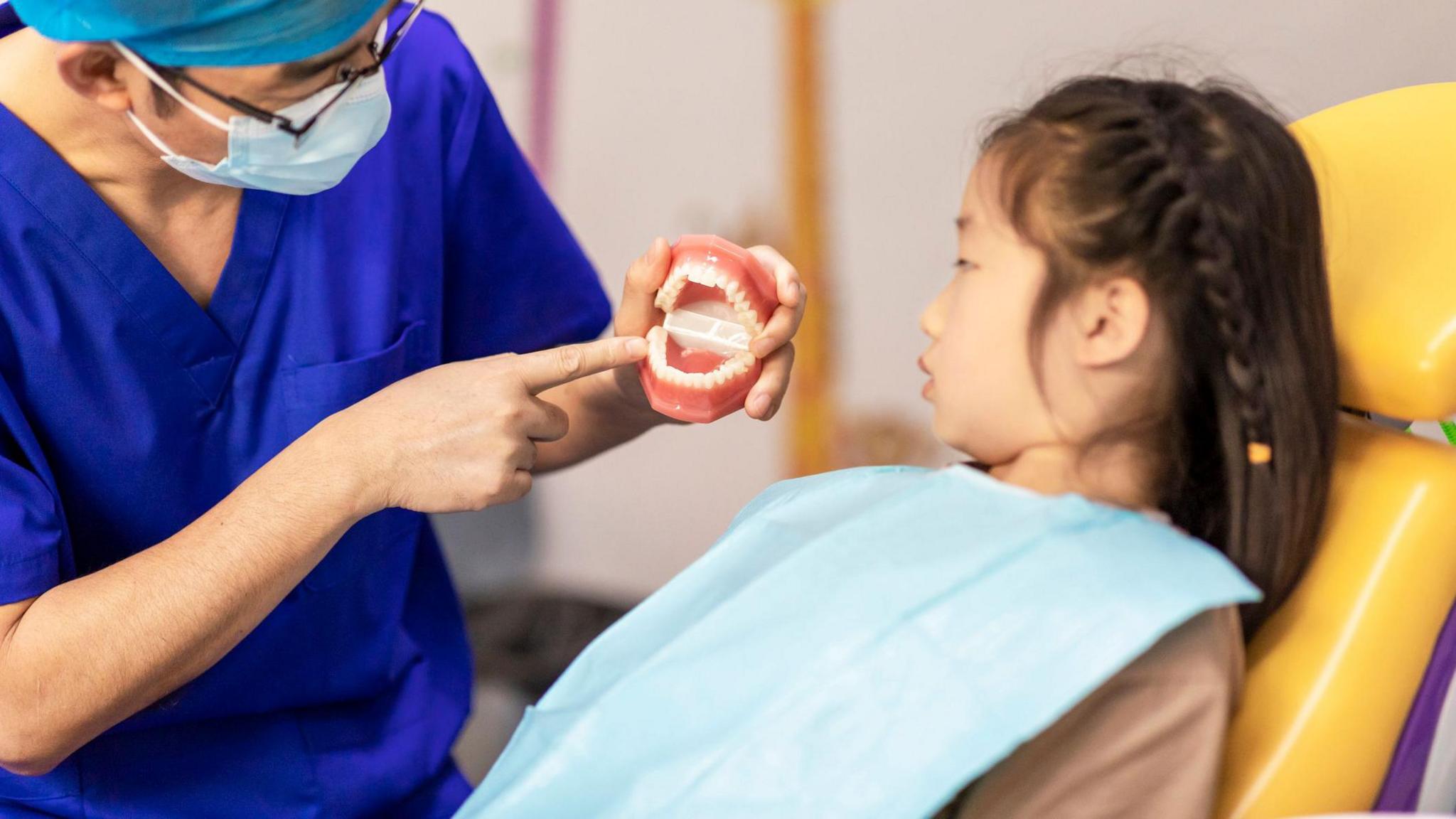 Child in the dentist's chair being shown false plastic teeth