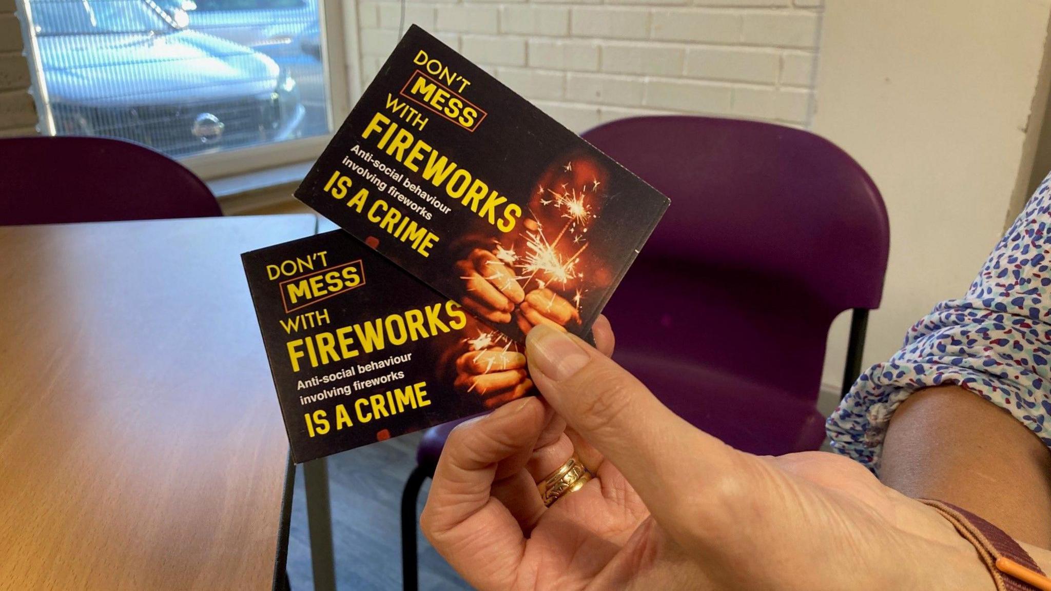 A woman's hand holding two of the bank card-sized Consequences Cards which have yellow writing on a dark background with a photo of someone burning a sparkler.  