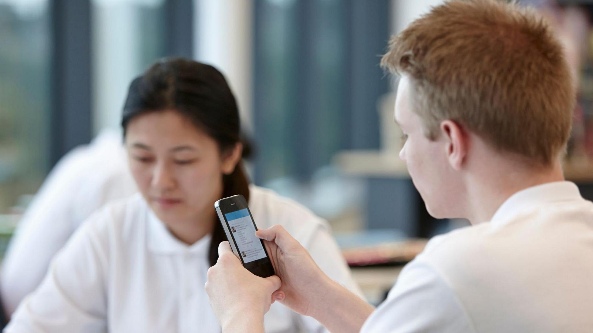 Teenage boy using cell phone in classroom (stock photo)