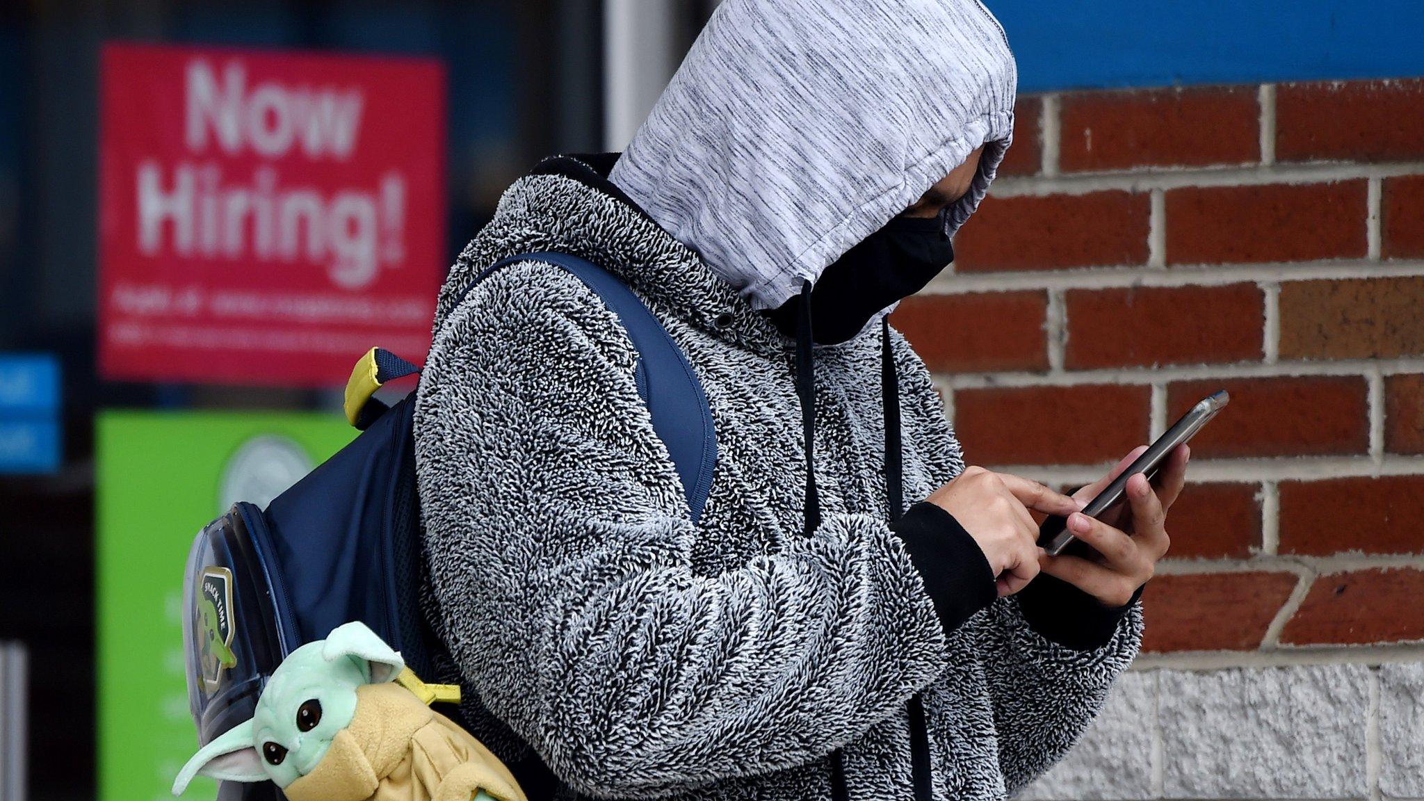 a person in a mask near a now hiring sign