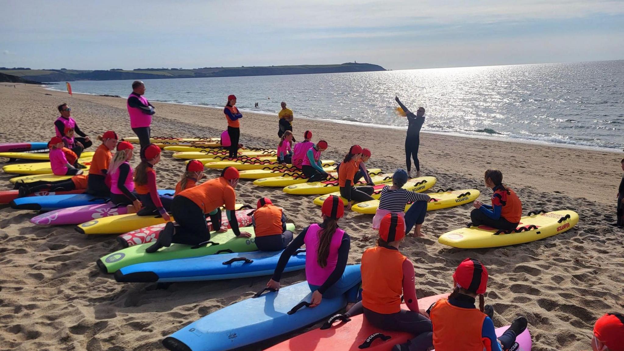 Young people with their surfboards listening to an instructor.