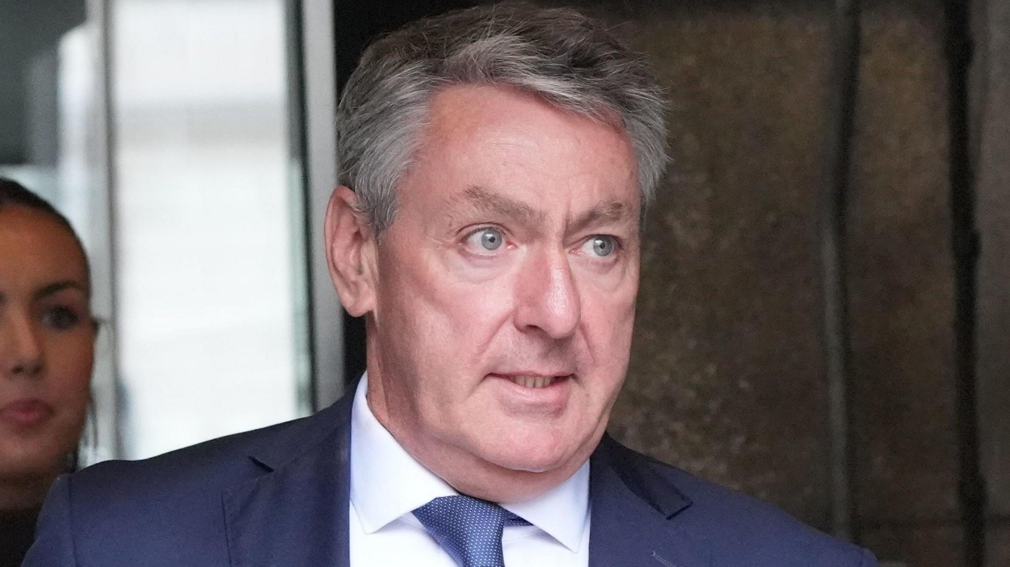 Billy Kelleher in a blue suit, white shirt and blue tie. He has grey hair.