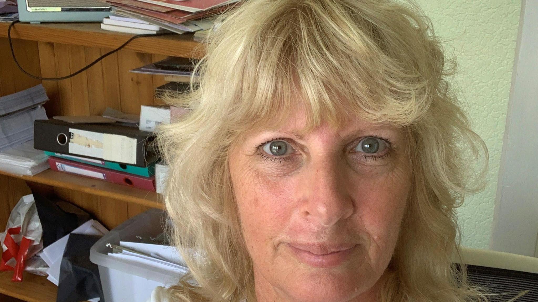 Eileen Lavelle, with pale blue/grey eyes and light blonde hair, sits in her office, surrounded by folders and boxes of notes.