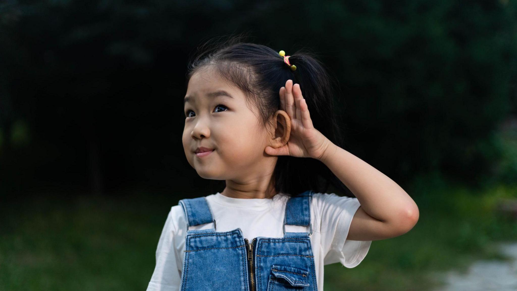 little girl holding hand to ear and listening