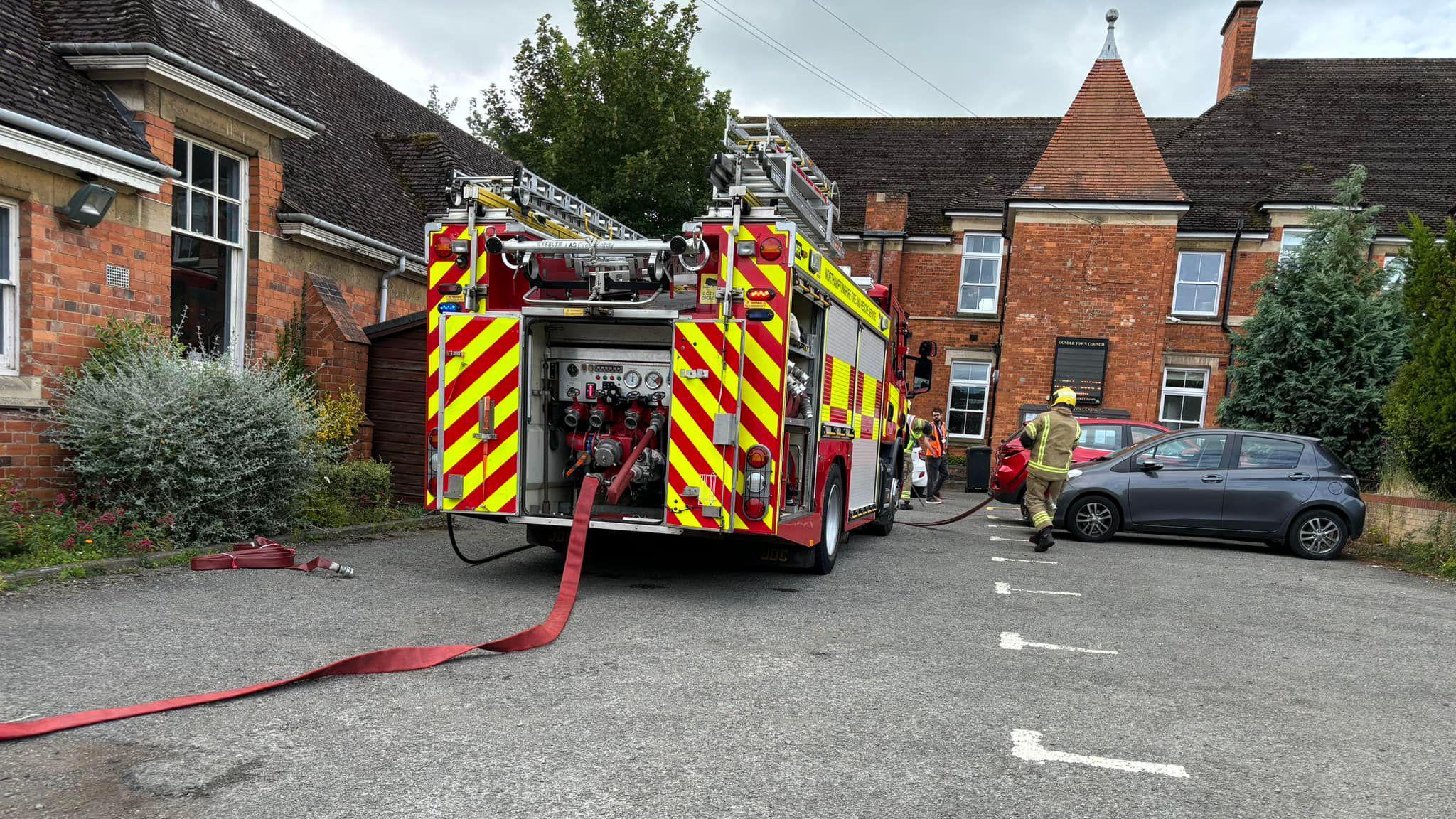 Brick library building with fire engine outside. A long red hose is visible in the foreground