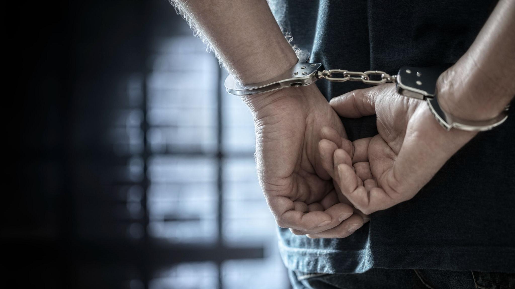 Close up of an arrested person with handcuffed hands behind their back.