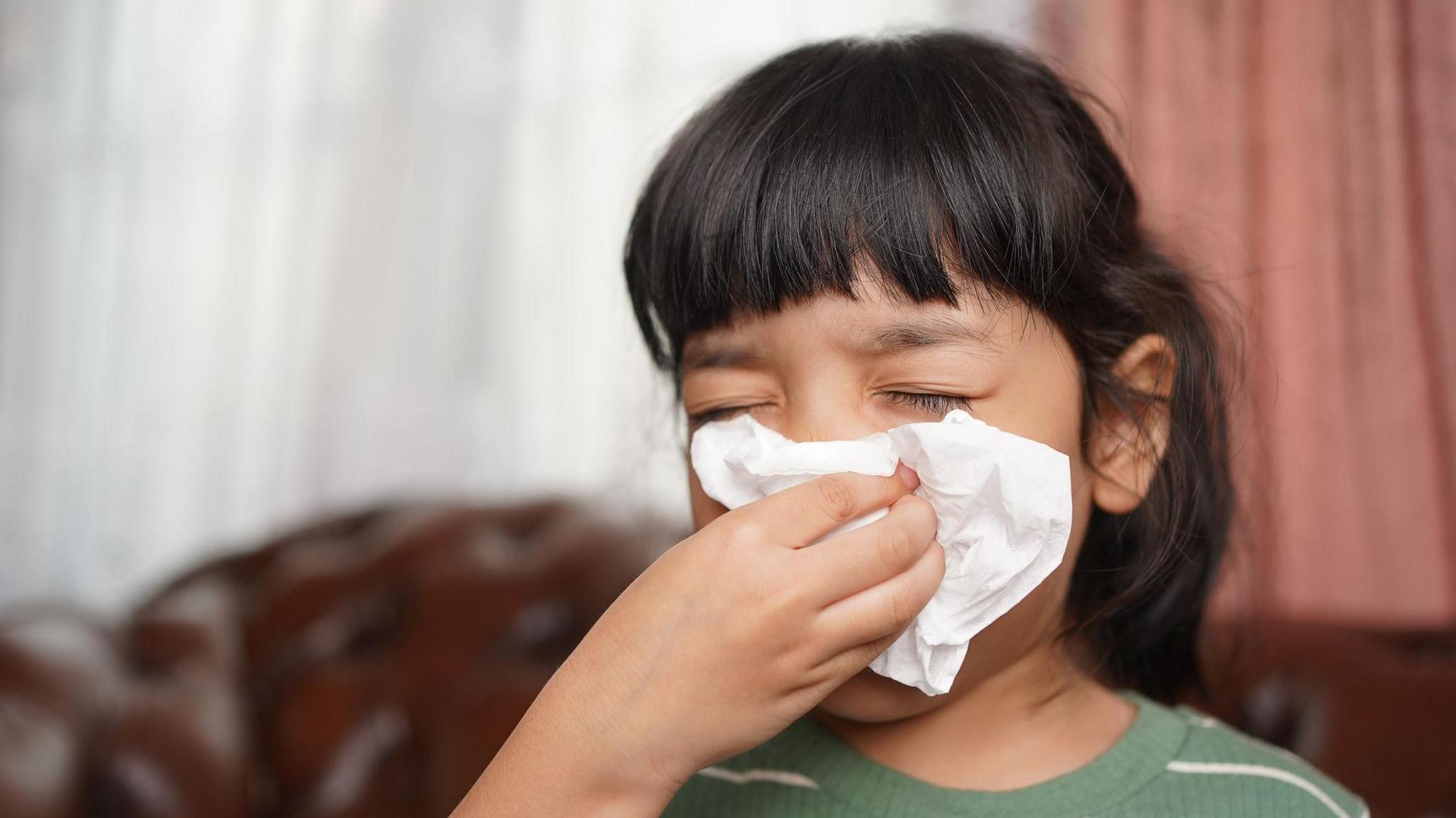 A girl blowing her nose on a tissue. 