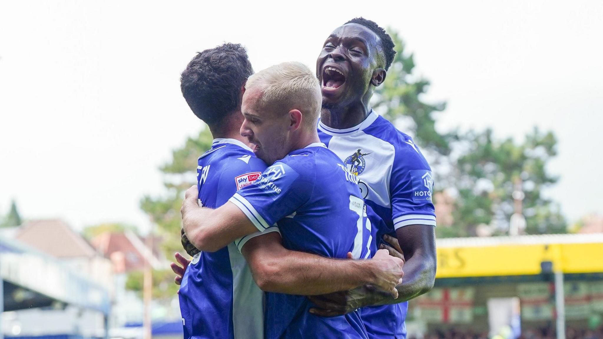 Three Bristol Rovers players embrace tightly as they celebrate a goal during their match with Barrow at the Memorial Stadium.