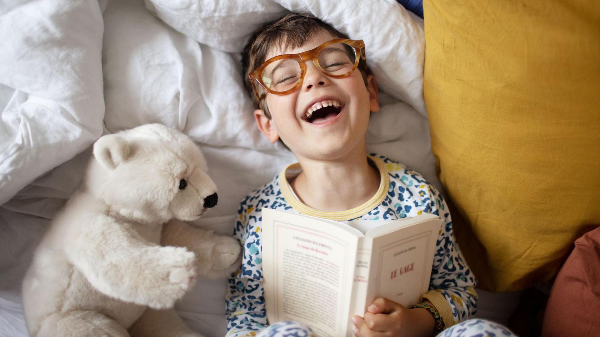 a boy reading a book in bed and laughing