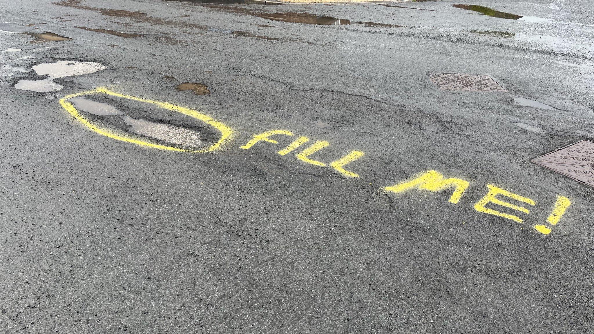 Graffiti next to pot holes on the road
