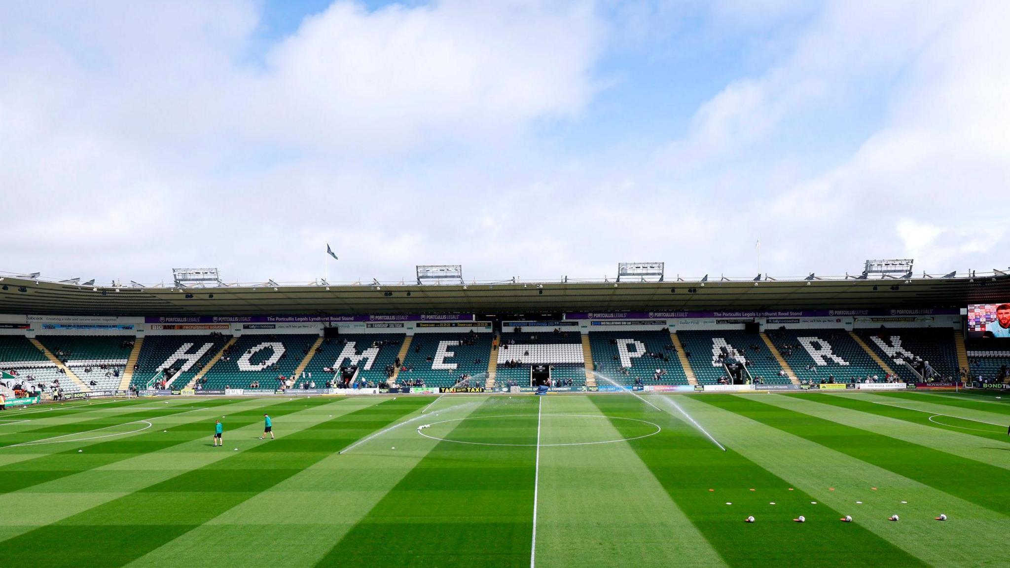 A general view of Home Park. There is a green pitch with people on it and in the background, in the stands is the words 'HOME PARK'