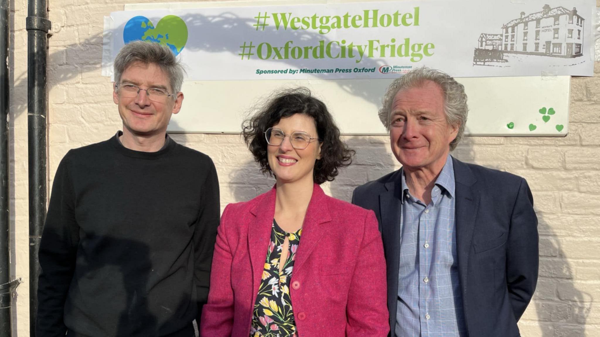 Oxford West and Abingdon MP Layla Moran and two men smiling for a picture on the day of the launch. A poster reading #WestgateHotel #OxfordCityFridge is on the wall behind them. It is sunny.