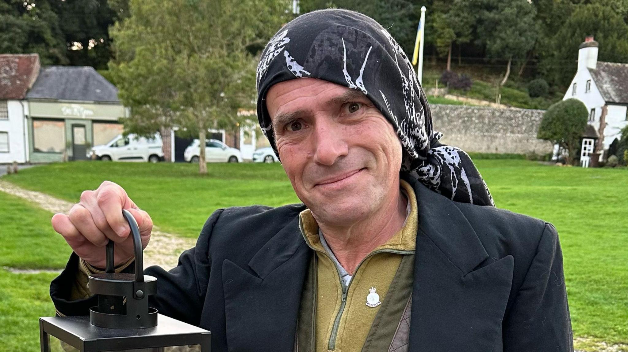 Larry Gray in a navy blazer and a black bandana looking at the camera while holding a lantern with a candle inside