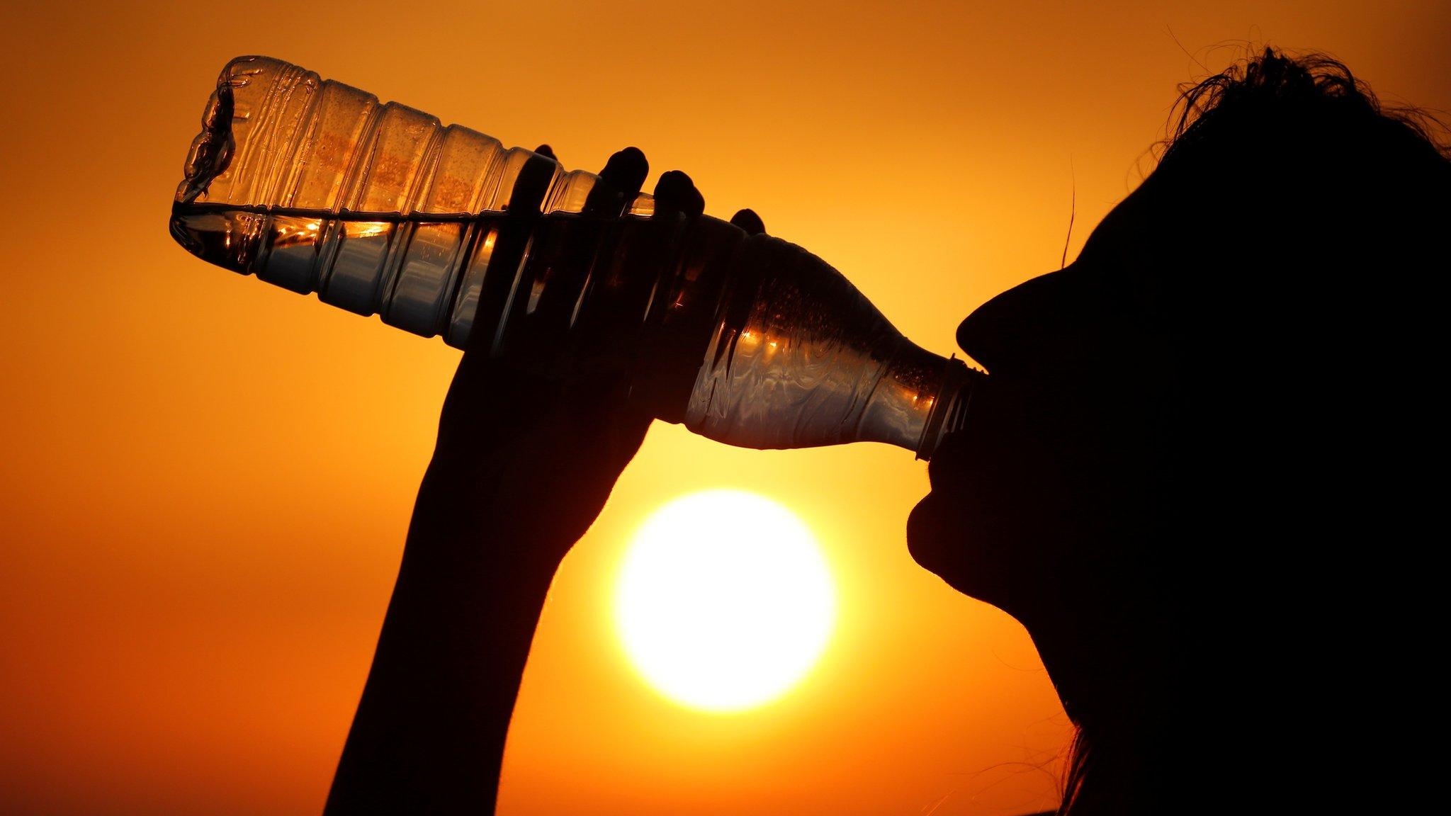 A woman drinks water during sunset, as a heatwave hits France, in Cagnicourt near Cambrai, France