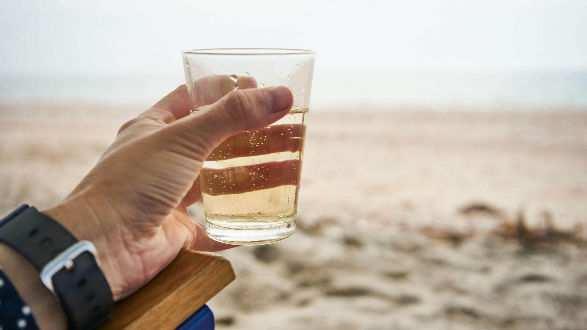 Hand holding glass of drink on beach