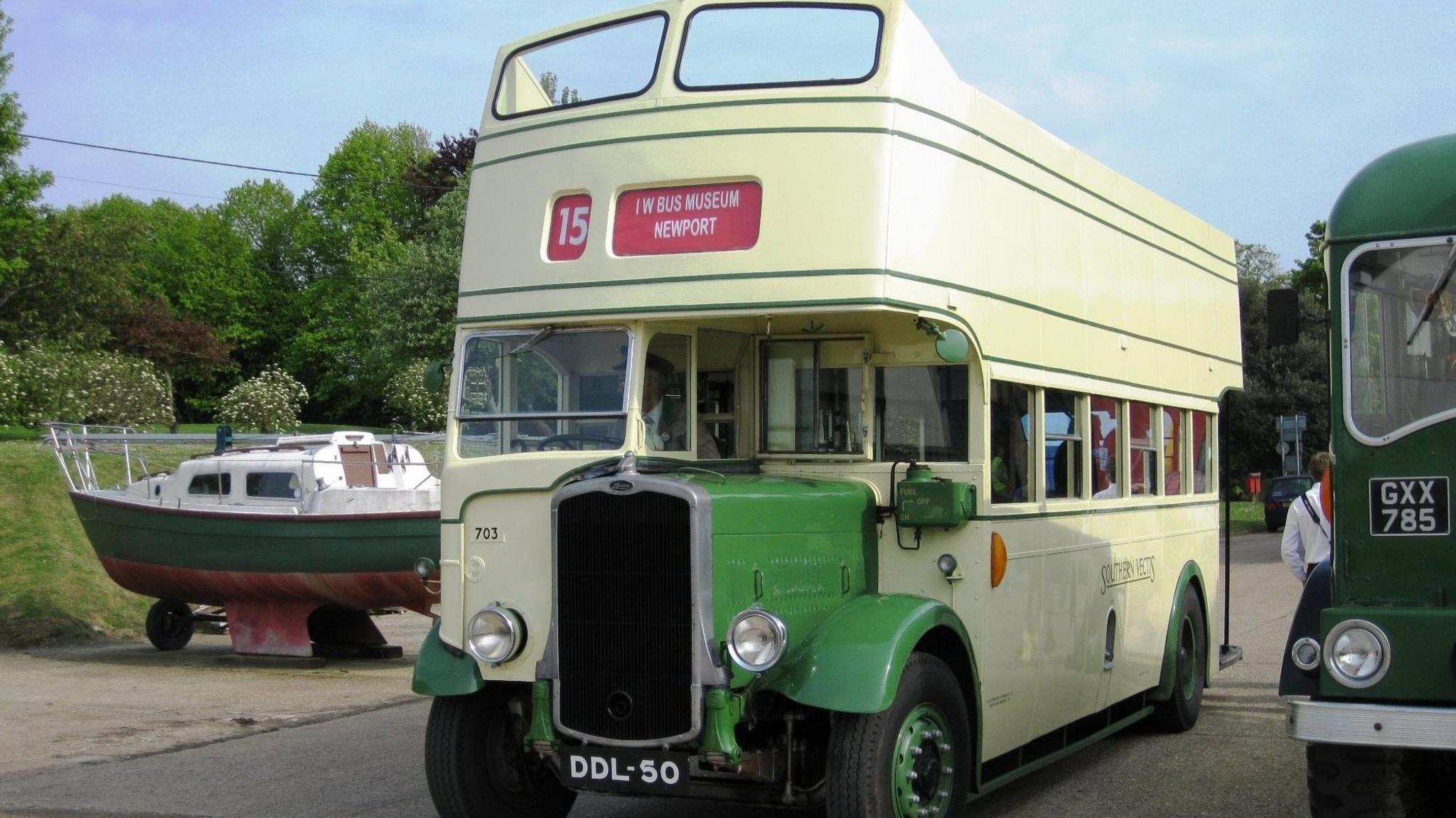 A light yellow DDL 50. There is another bus next to it and a boat. There are a driver and passengers inside.