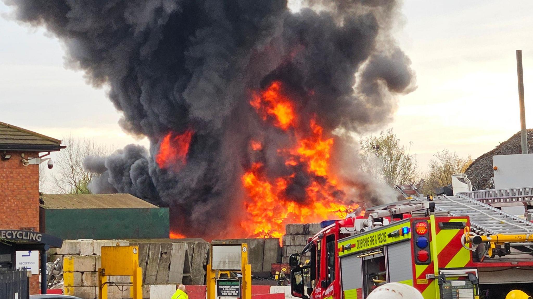 The top of a fire engine can be seen in the foreground with a large orange blaze in the background.