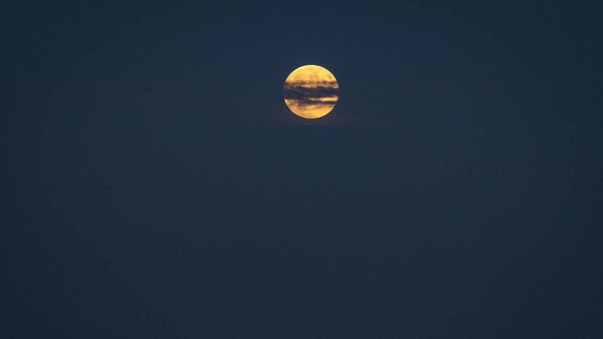 An orange moon in the distance behind a thin line of dark cloud across its centre