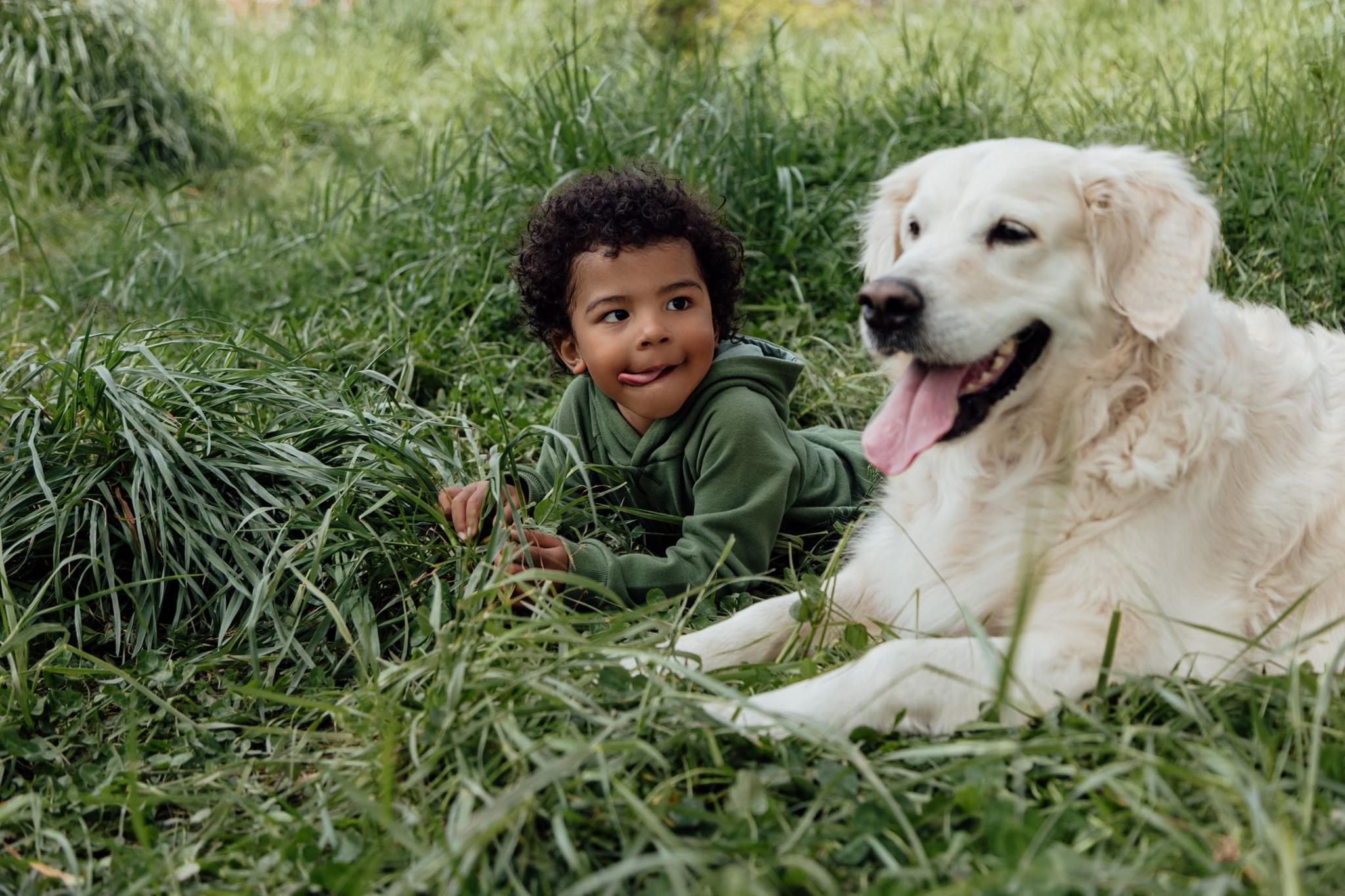 child sticking tongue out sat next to a dog with its tongue out. 