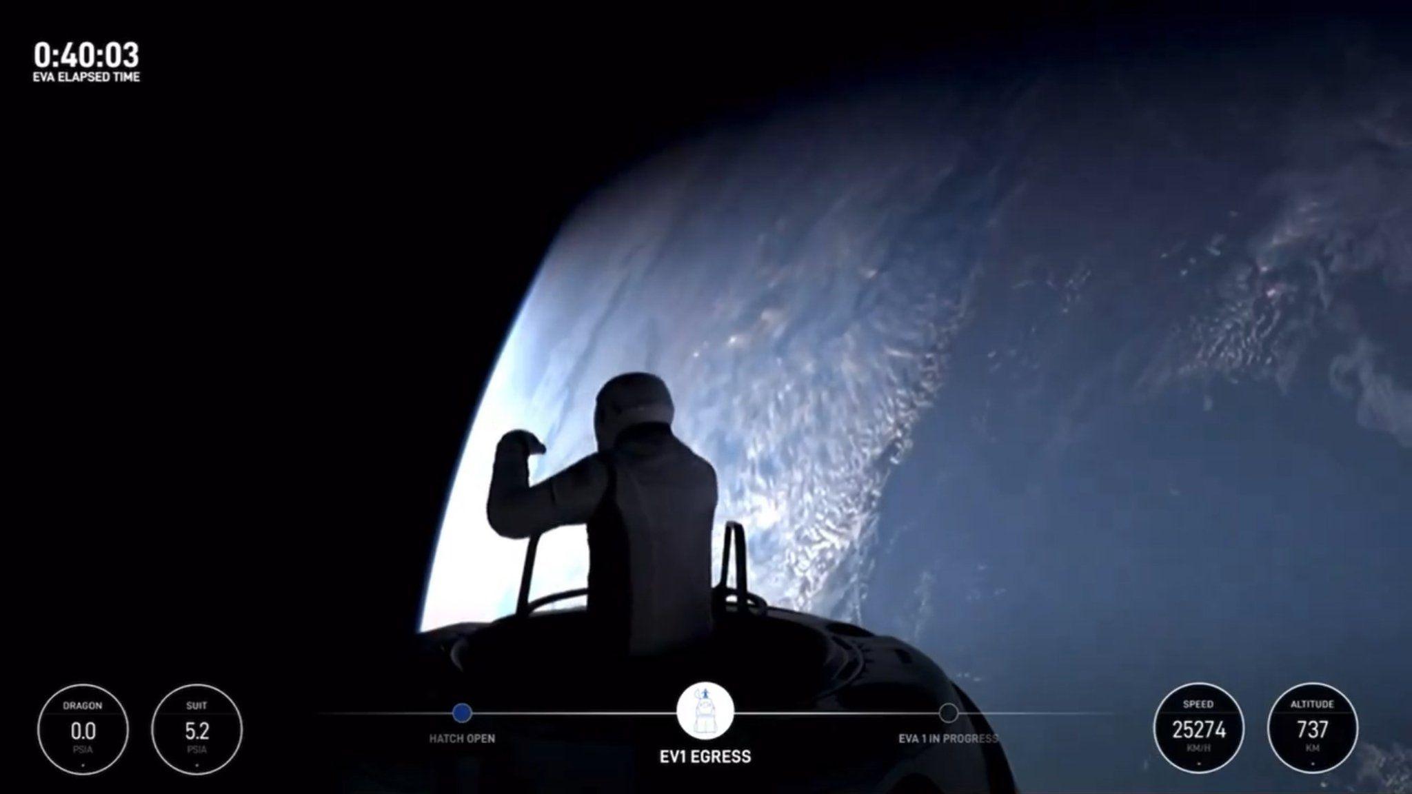 Jared Isaacman steps out of the hatch of a spacecraft at the start of the first private spacewalk. He in shadow, wearing a spacesuit. The Earth can be seen in the background on the right-hand side of the picture. It is blue and curved and white cloud can be seen.