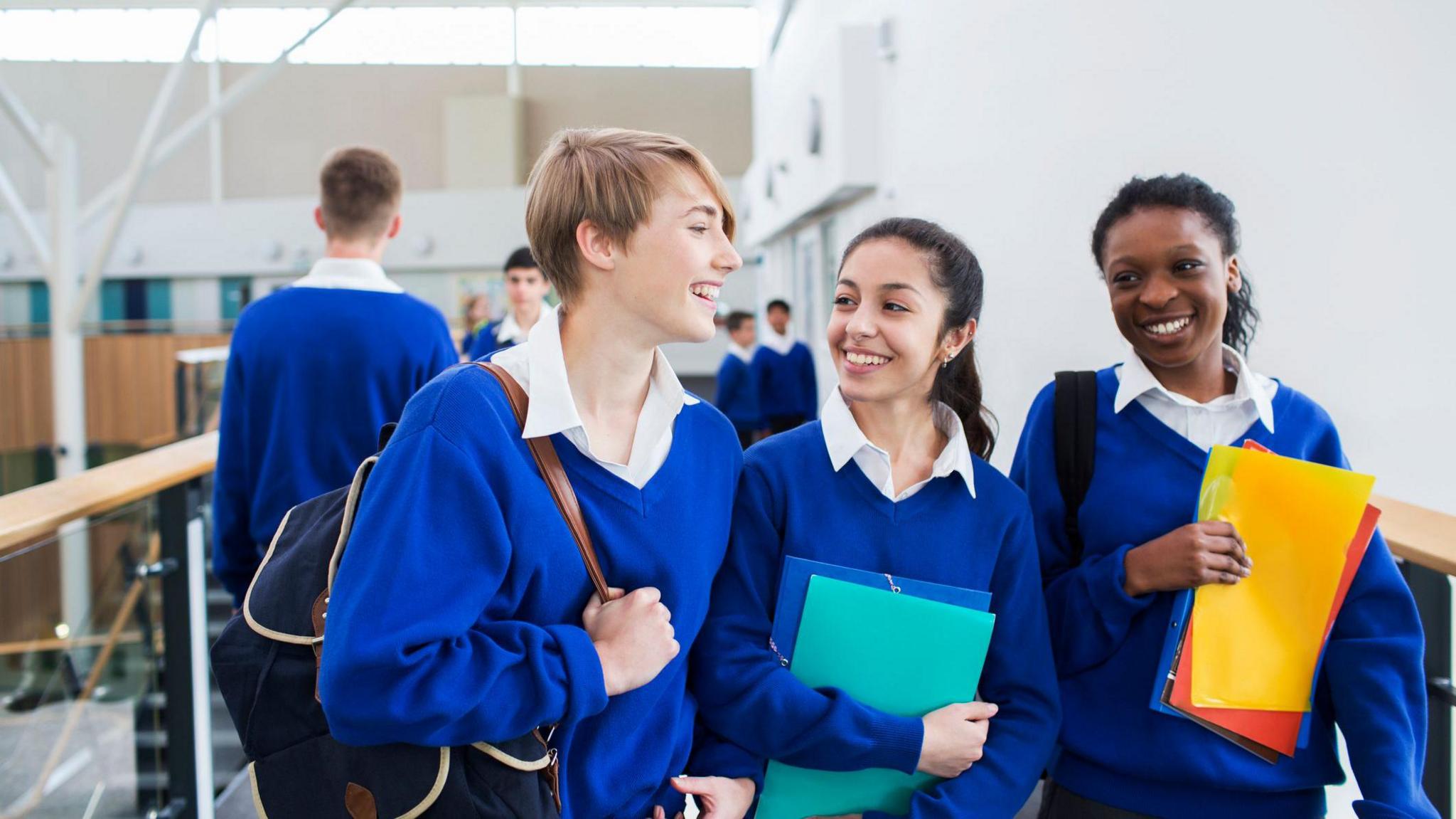 Three teenagers in secondary school uniform walking in a school corridor holding folders