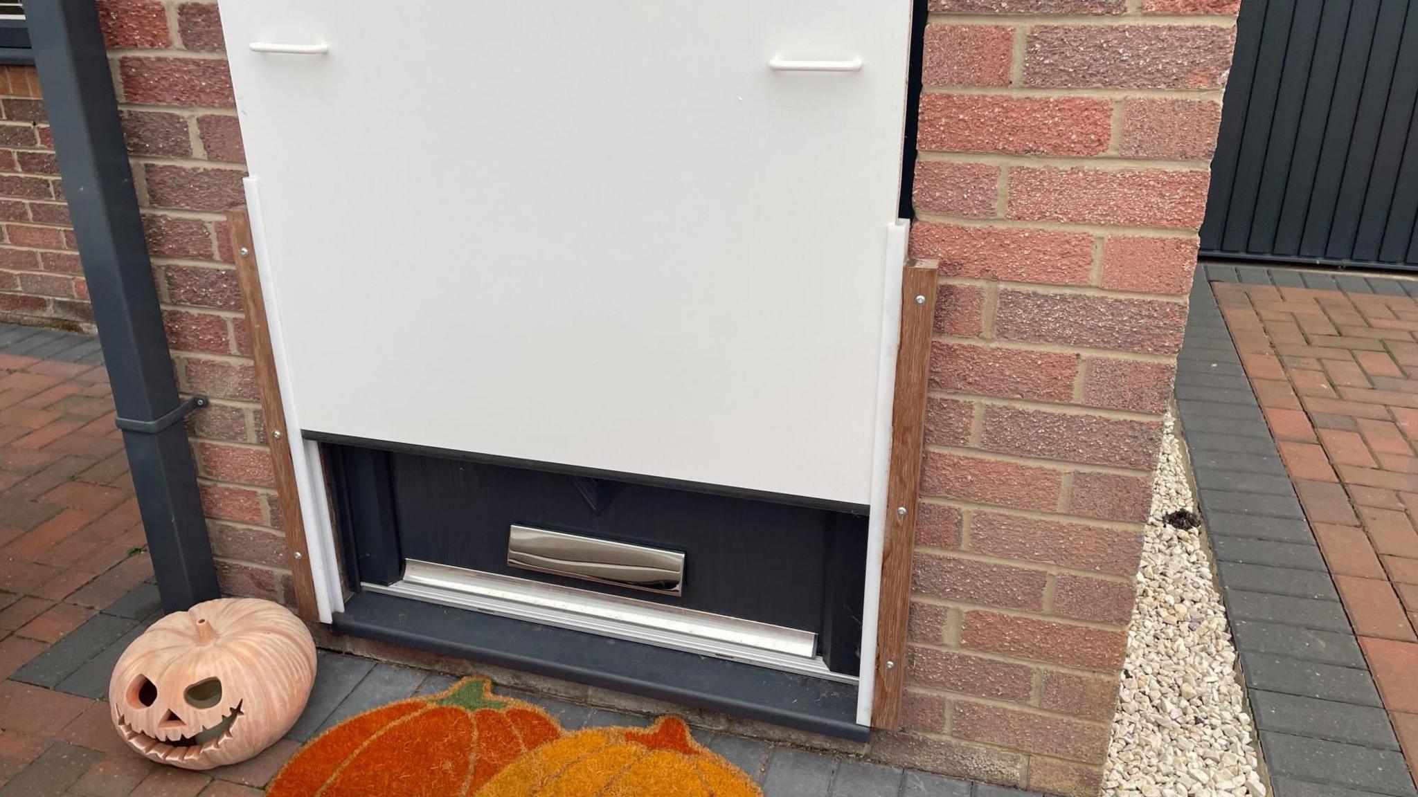 A front door with a carved pumpkin and pumpkin mat outside. The door also has an extra white barrier sheet on the bottom half with two white handles.