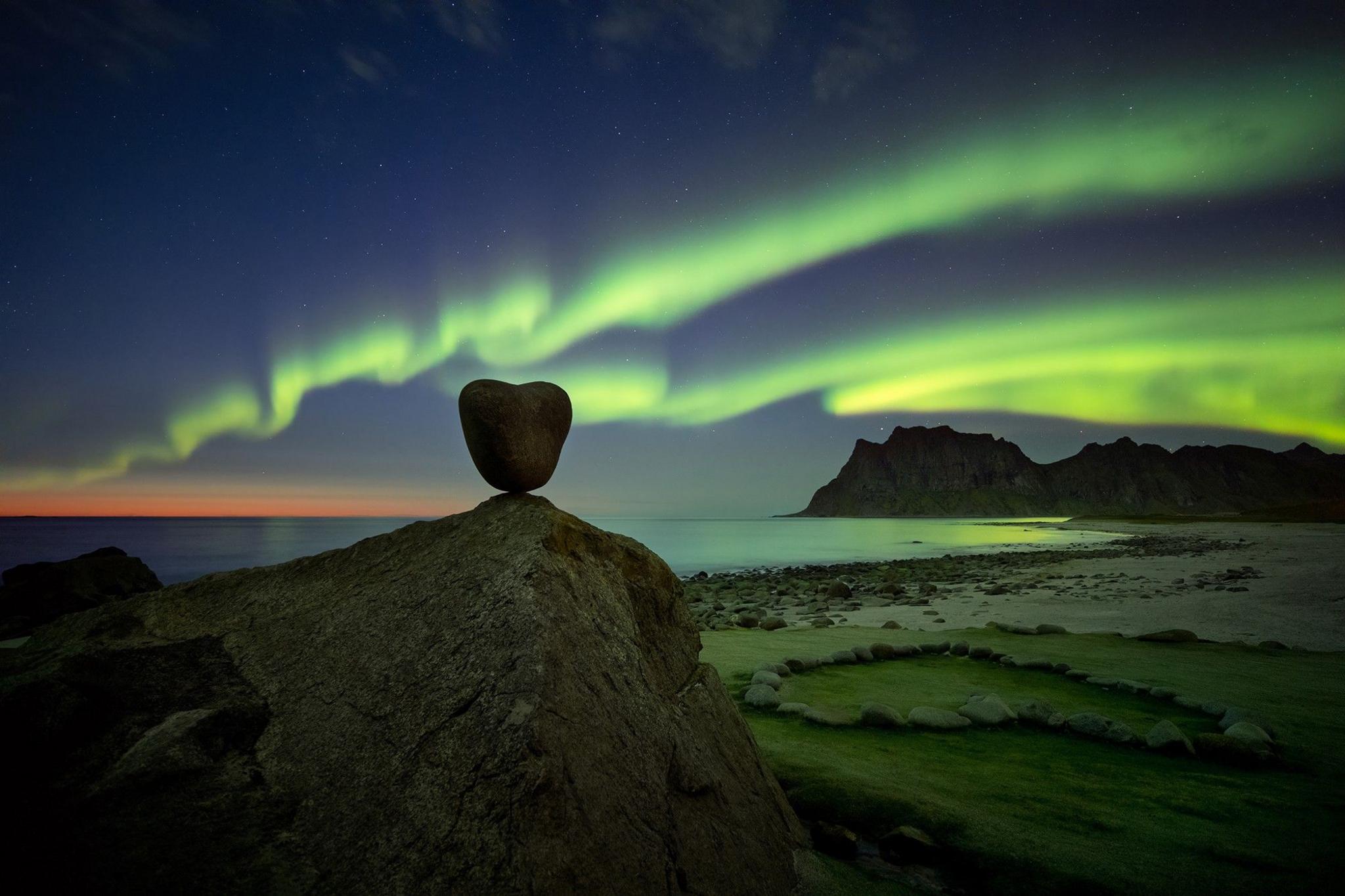 The aurora in the night sky behind a heart shaped rock