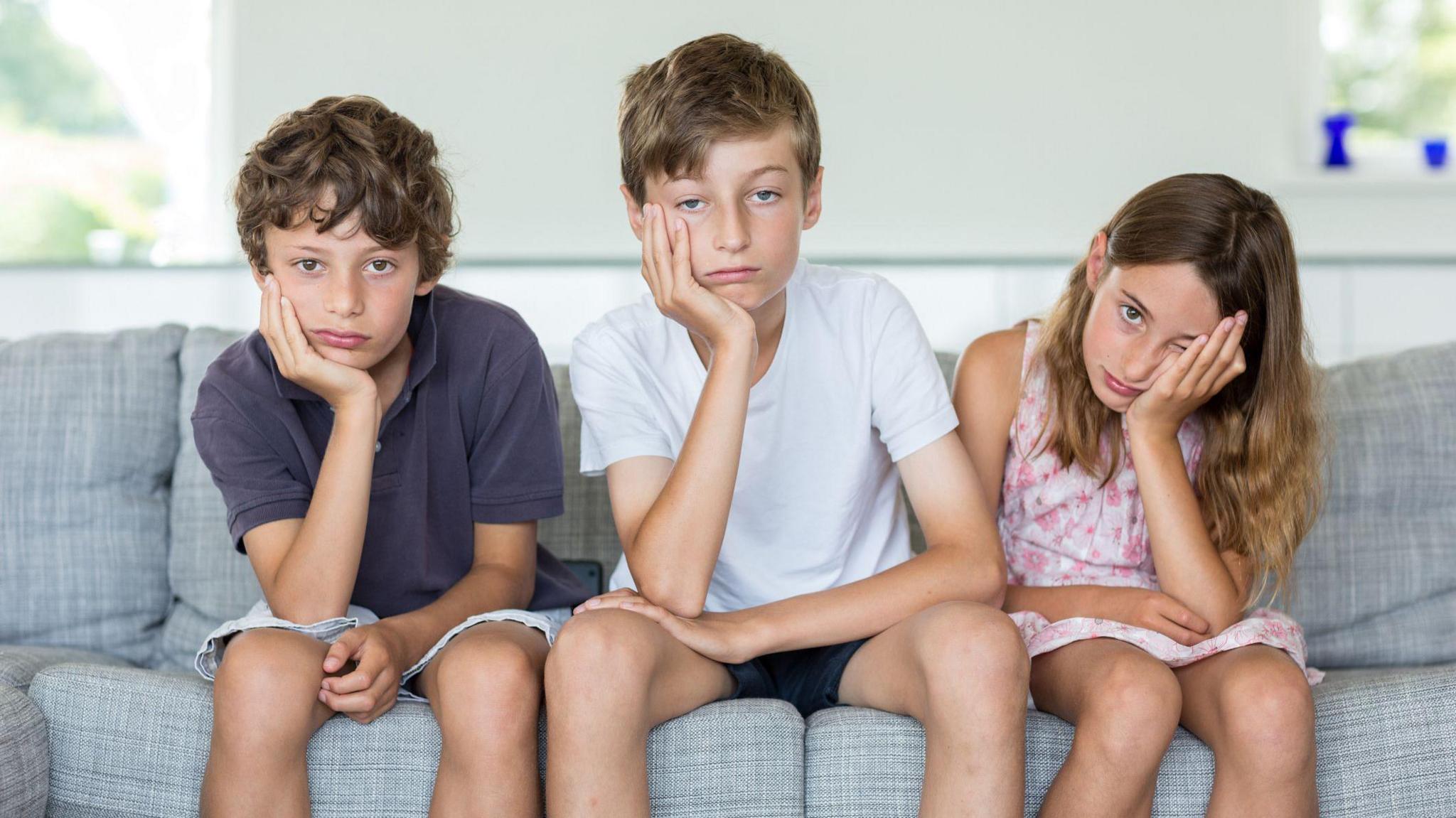 there kids sitting on the sofa looking bored at the camera