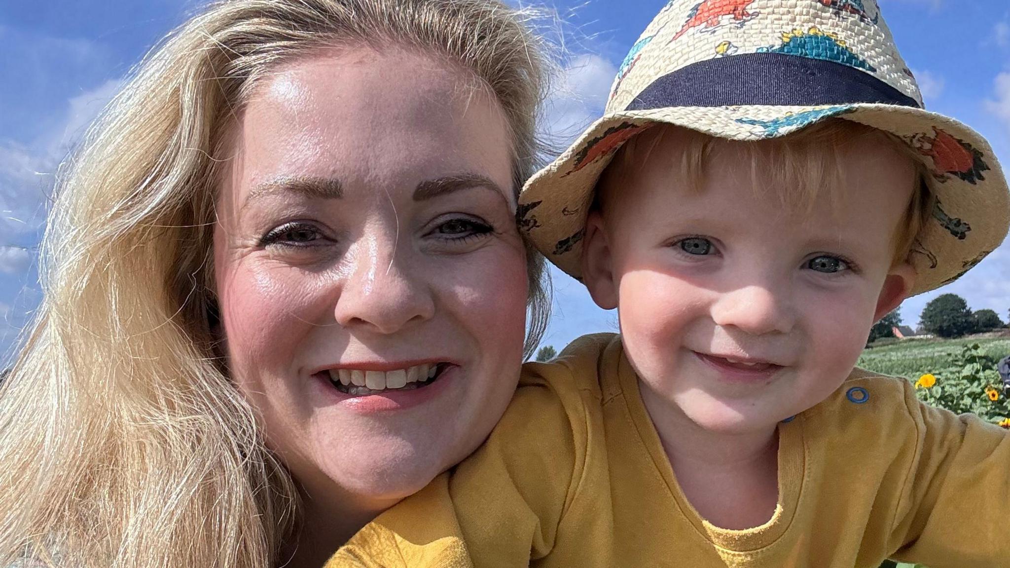 Kristal and her son Austin smiling at the camera. Austin is wearing a yellow top and sunhat