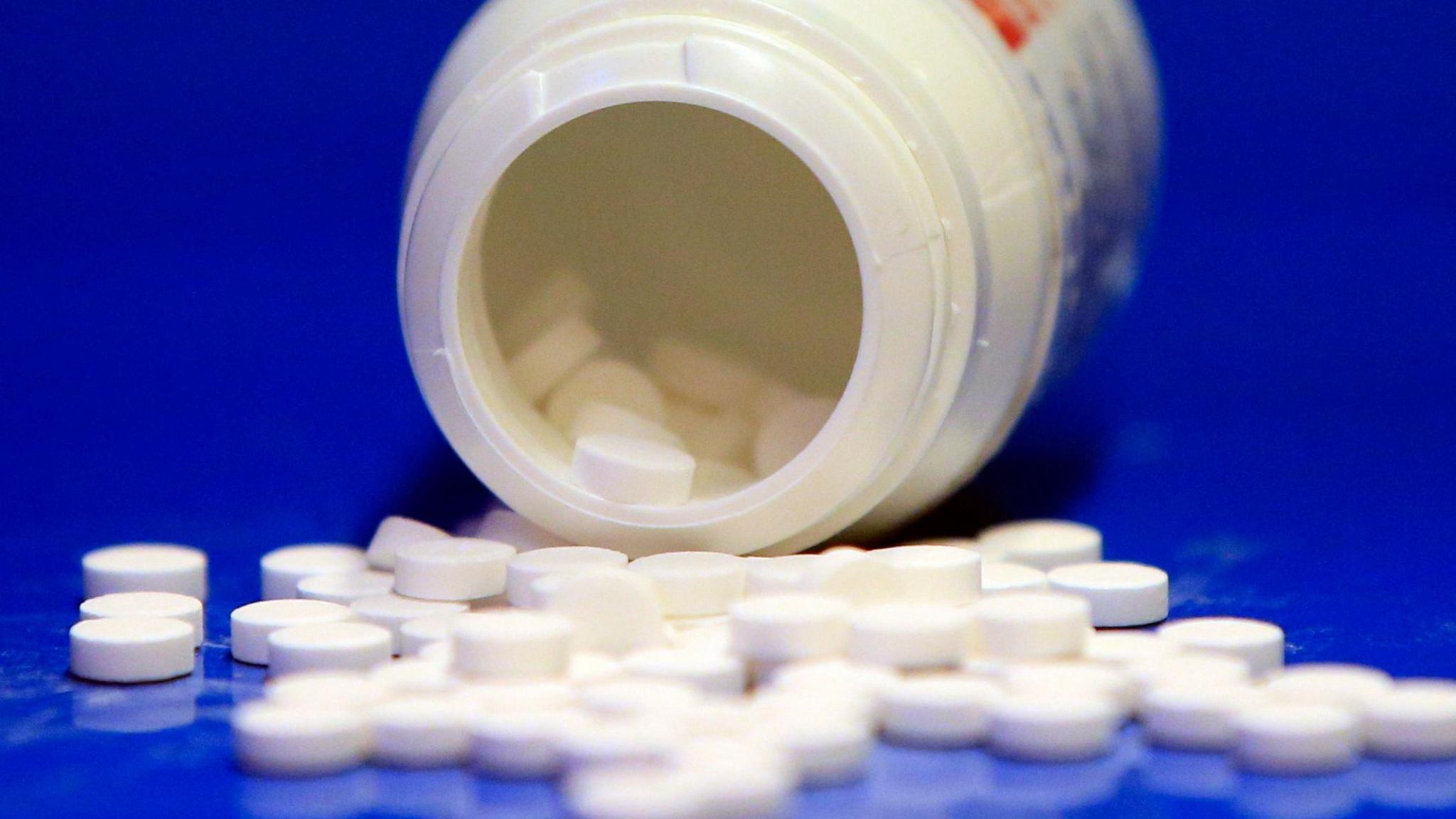 A generic view of medical tablets that are spilled out on to a blue surface. The bottle can be seen on its side as tablets spill out. 