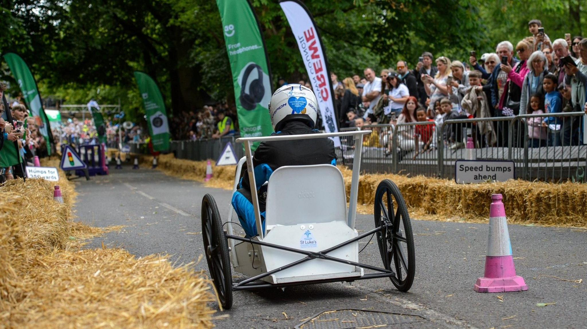 The back of a white go-kart that is racing through a street. Crowds are cheering on either side of the road.