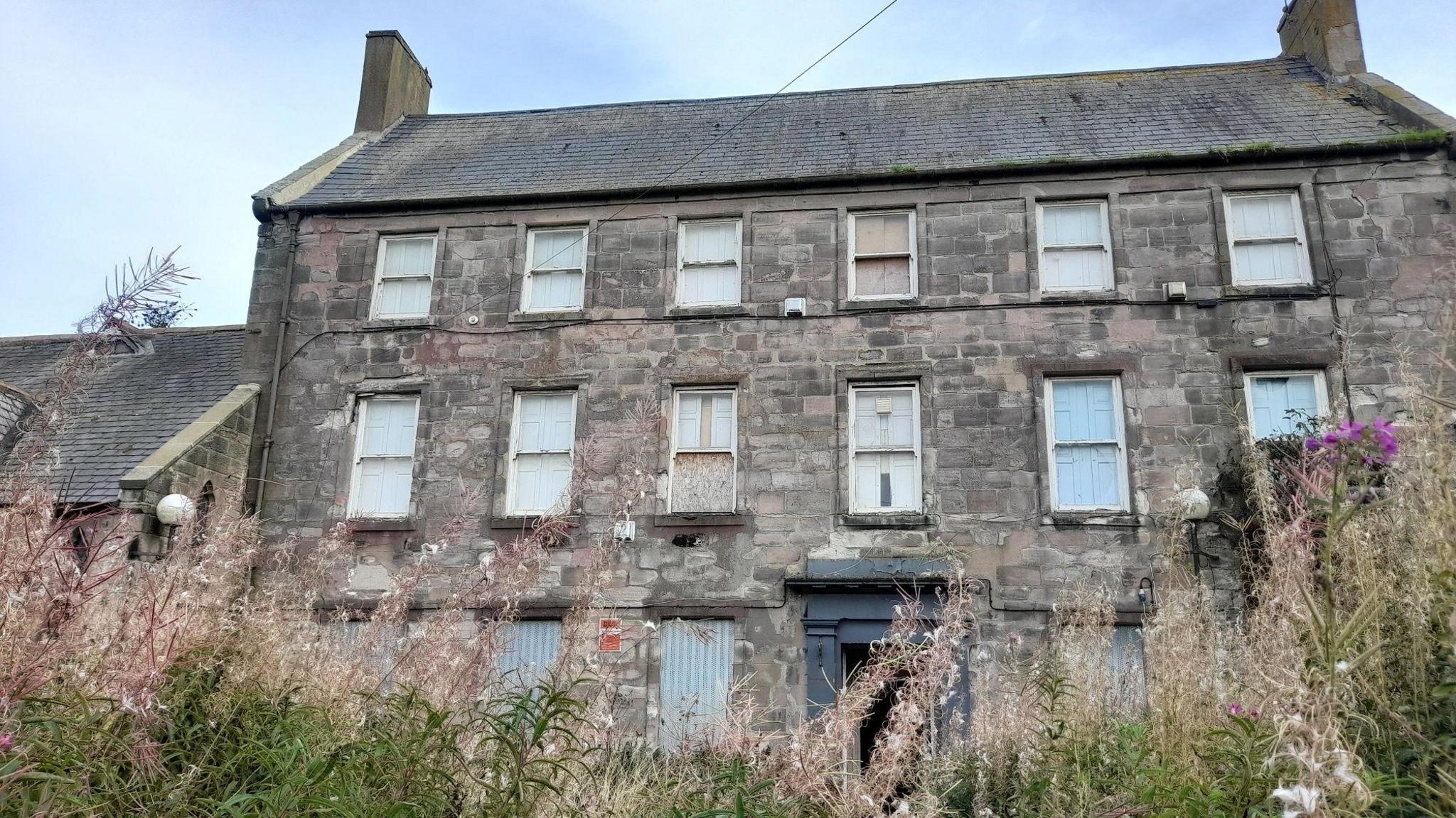 A Georgian mansion house, dating back to 1754, and the former site of Berwick Grammar School, in a state of disrepair. It is a three-storey building with boarded up windows.