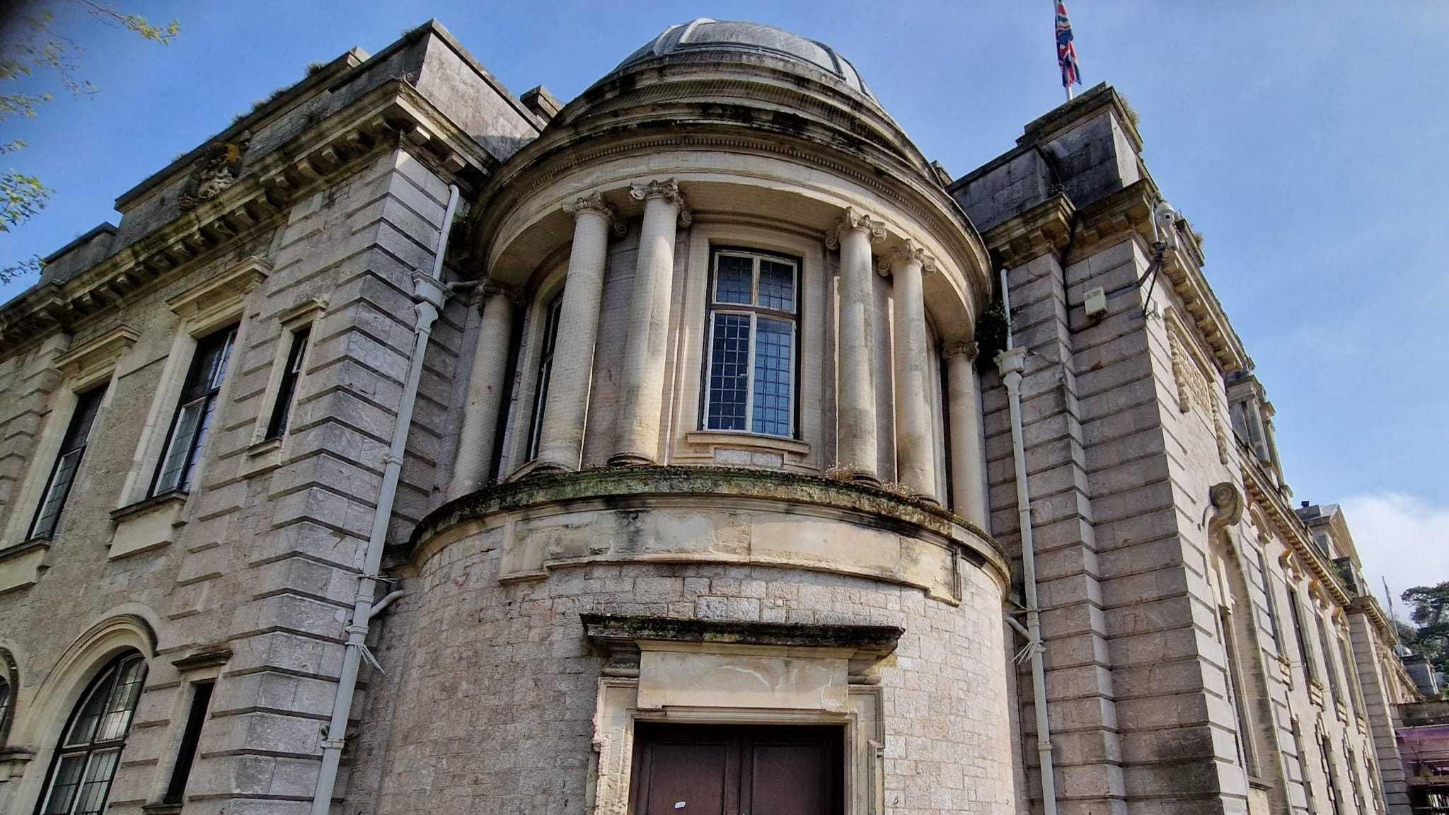 The front of the Torquay Town Hall. The building is light grey and there is a window above the doorway. On both sides of the building there are a number of windows.