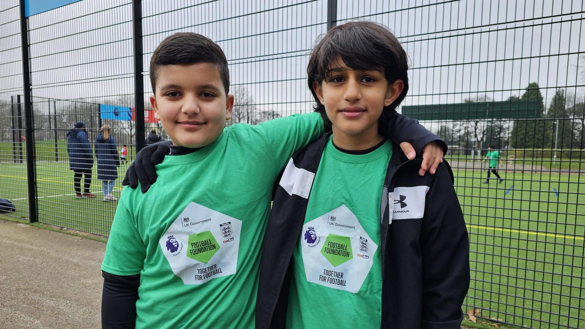 Romeo and Daud standing in front of the new pitch while their friends play football in the background