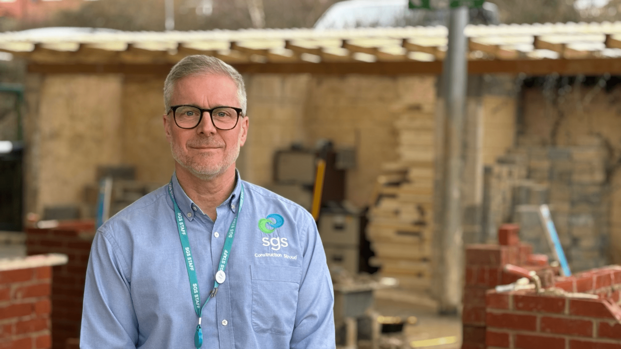 David Quinton wearing a blue shirt, standing in a brick yard, looking at the camera