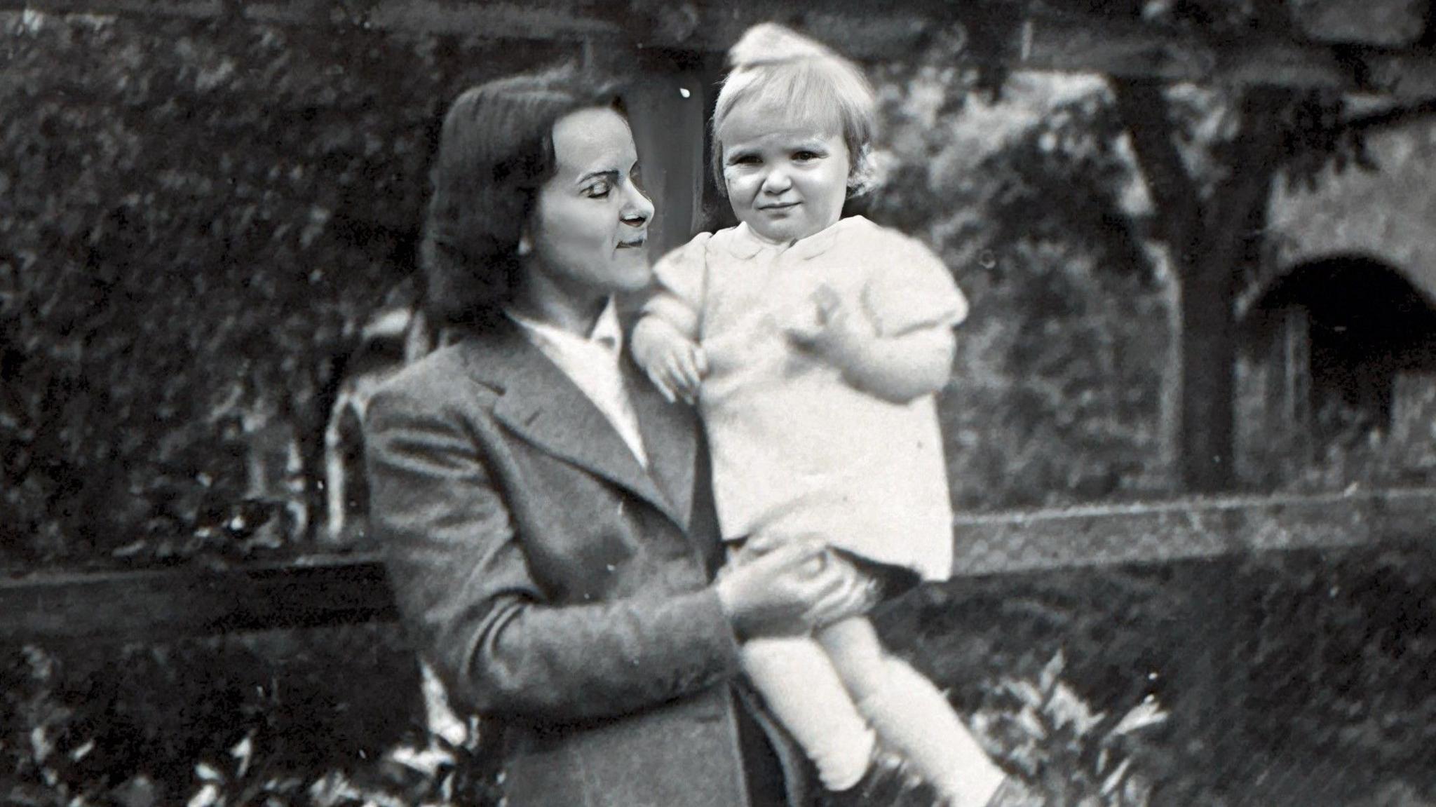 A black and white photo of a woman holding a young child. The woman is wearing late 1940s clothing.