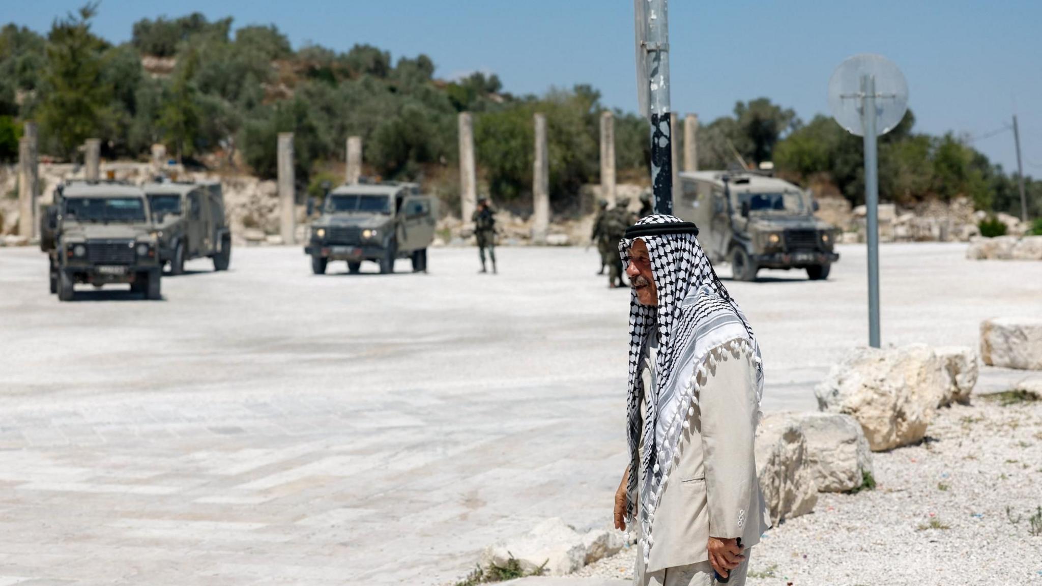 A Palestinian man walks near Israeli troops at the archaeological site of Sebastia, in the occupied West Bank (29 June 2026)