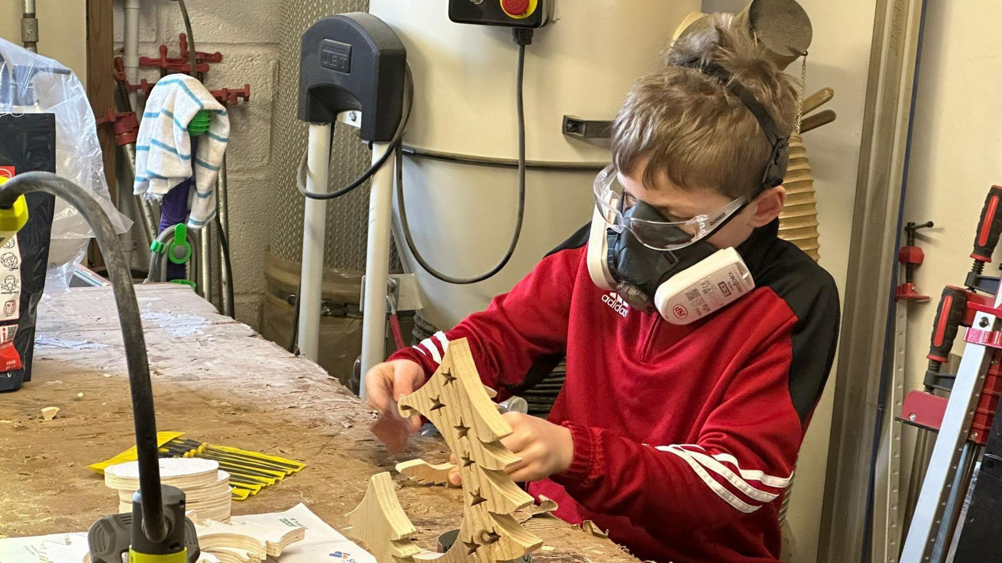 Alfie crafts a wooden Christmas tree in a workshop wearing a protective mask.