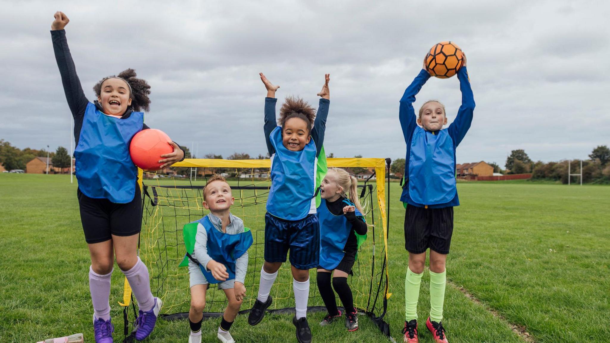 a small group of boys and girls wearing sports clothing, football boots and a sports bib on a football pitch.