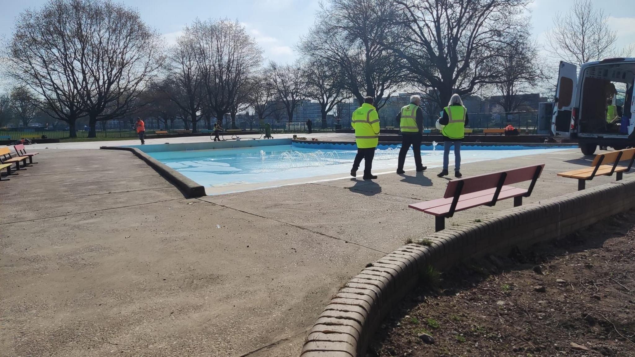 Three people in hi-vis vests looking at work progressing on the paddling pool