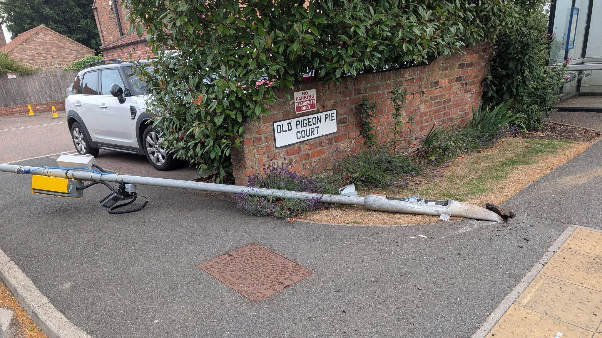 A yellow box attached to a lamp-post is pictured bent over and lying almost horizontally on the ground.