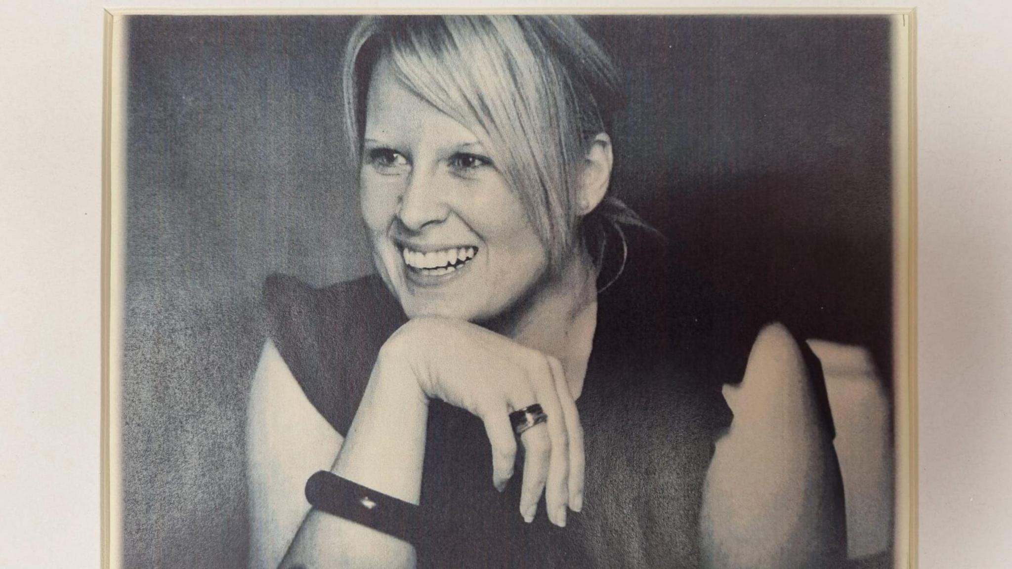 A black and white photograph of Charlotte Conlon, she is resting her head on the back of her hand and smiling