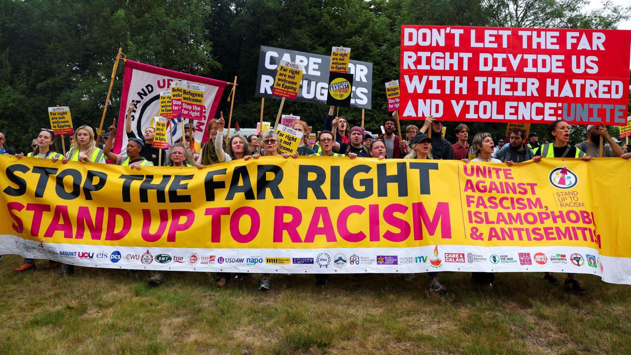 A large banner being held up by a lot of people, it reads 'Stop the far right. Stand up to racism.