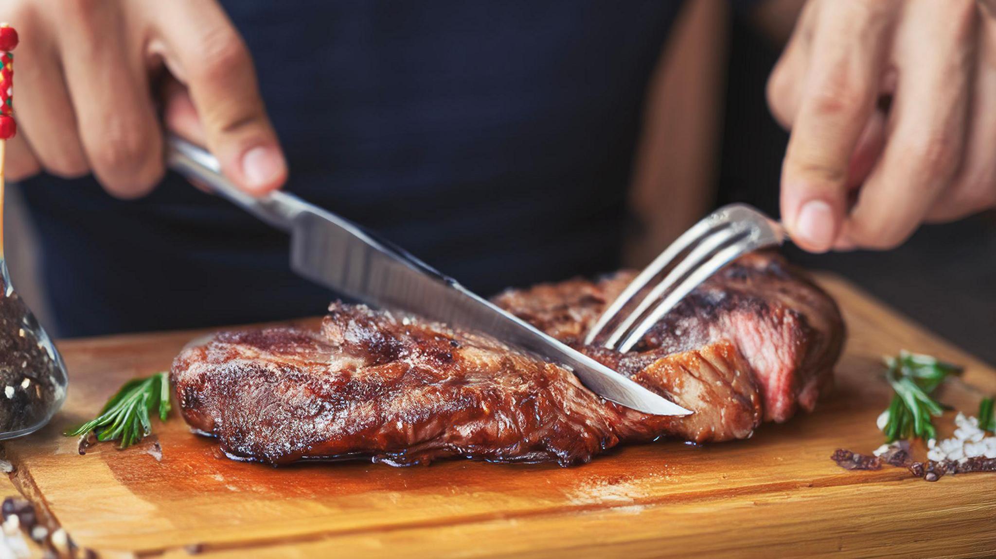 A person cuts into a steak that's presented on a wooden board