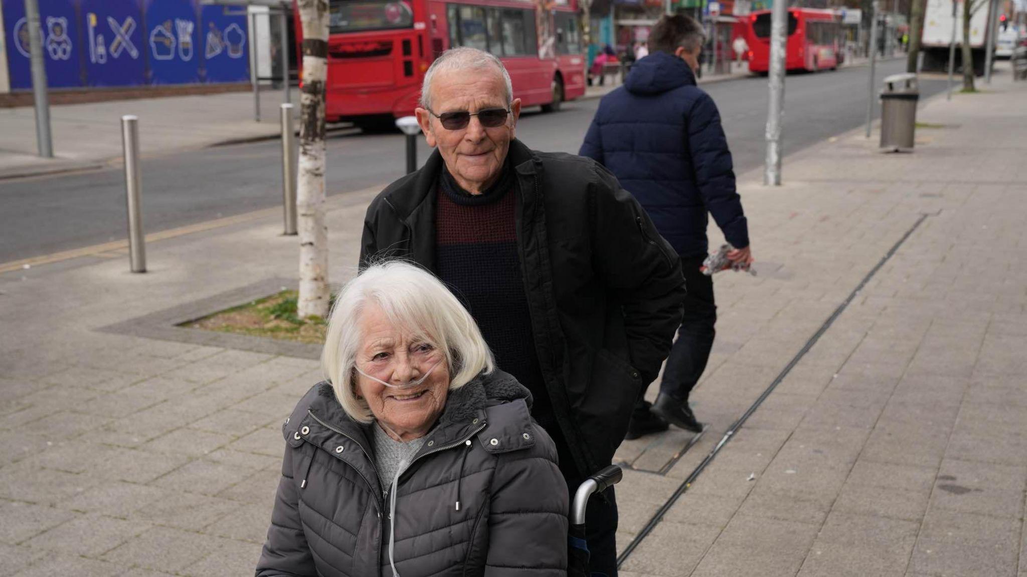 Maureen and Rod Saunders in Clacton town centre. Maureen is sitting in a wheelchair and Rod is standing behind her holding the handles of the wheelchair. 