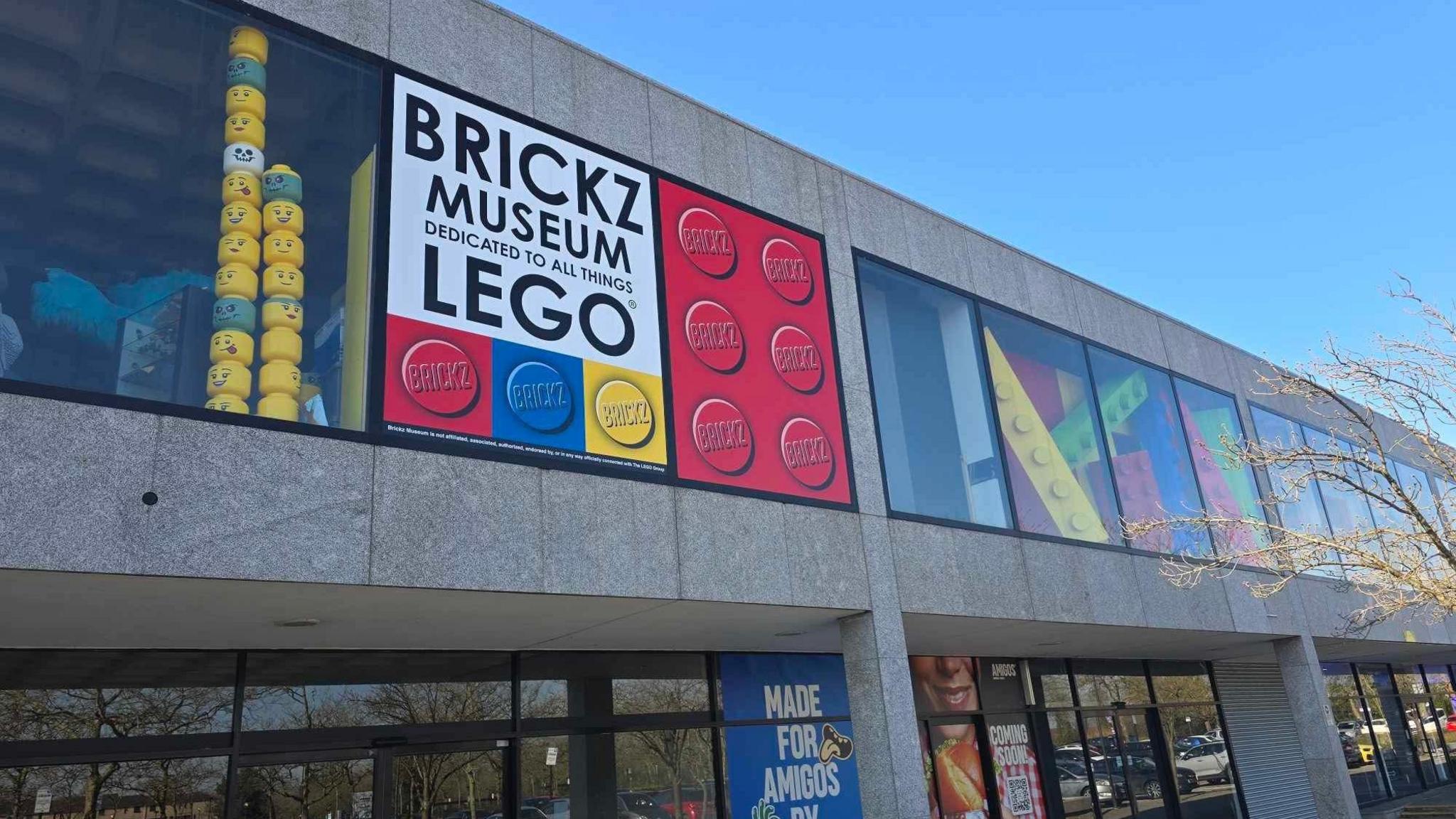 The outside of Brickz Museum in Milton Keynes. It is a grey concrete building, with a large "Brickz Museum" sign and large Lego structures on show behind the windows.