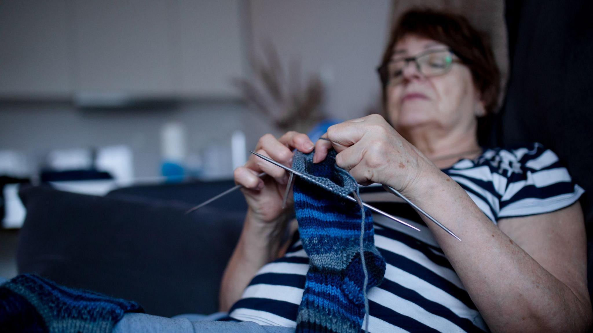 An older women knitting a blue and grey sock