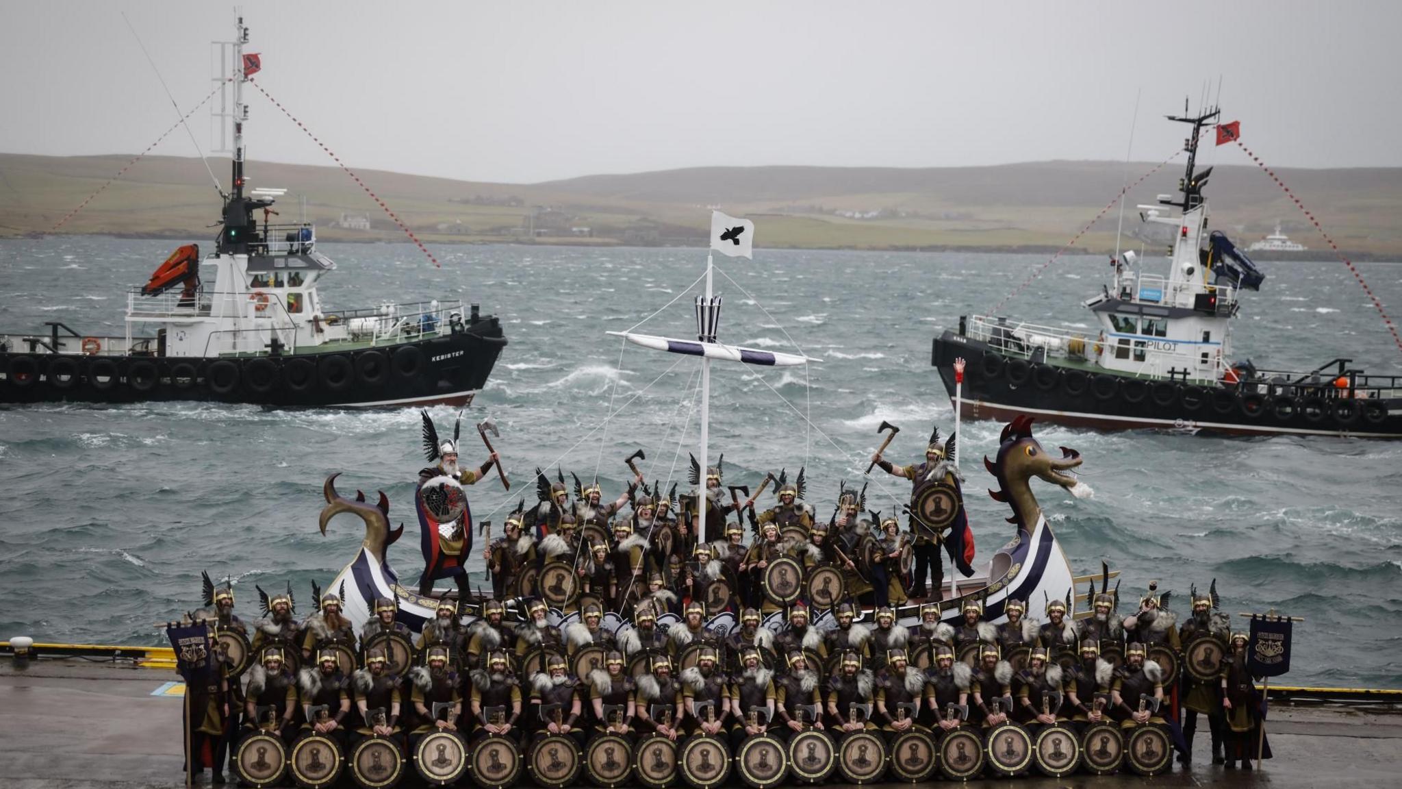 Members of the Up Helly Aa festival's 'Jarl Squad' pose with the replica Viking longship after the morning parade in Lerwick, Shetland Islands. There are also two fishing boats on the picture.