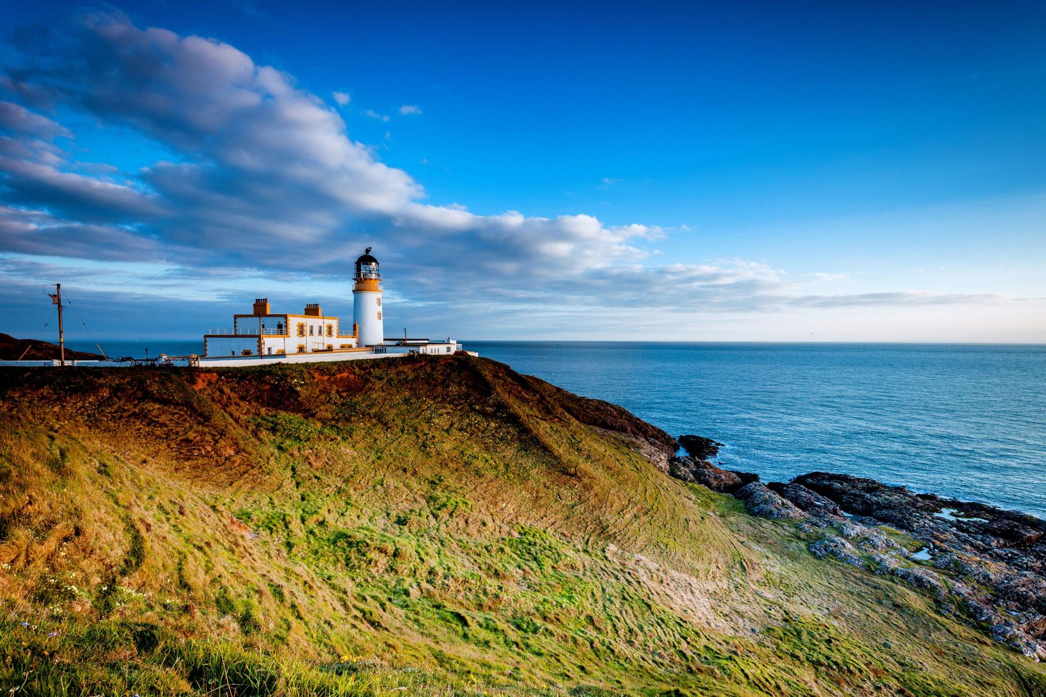 A lighthouse in the south of Scotland - it is a white and orange building on a grassy and rocky headland looking out over the sea